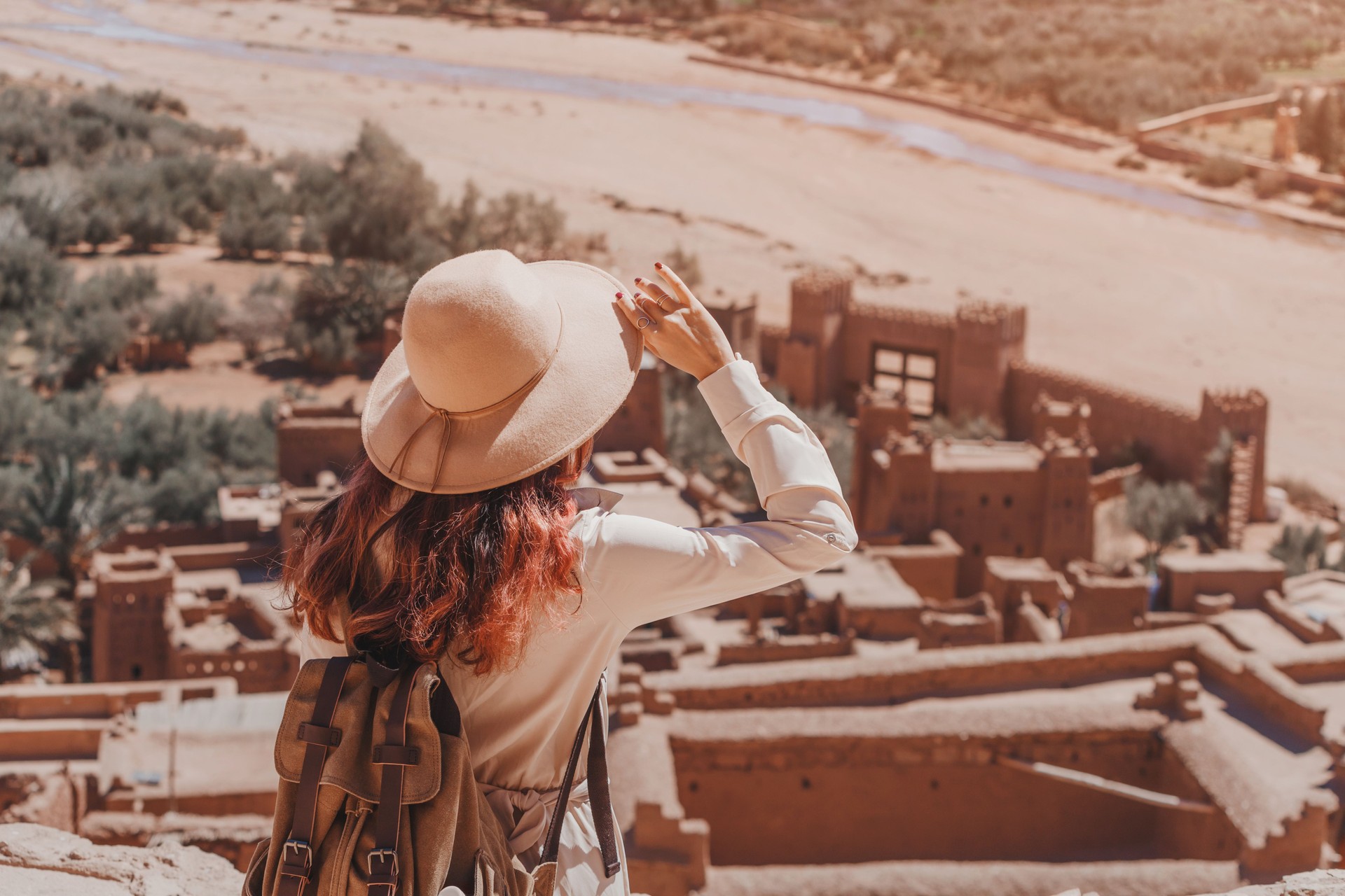 Female tourist holding her hat and admiring the landscape over Ait Benhaddou Ksar, an ancient fortified city in Morocco, near Ouarzazate